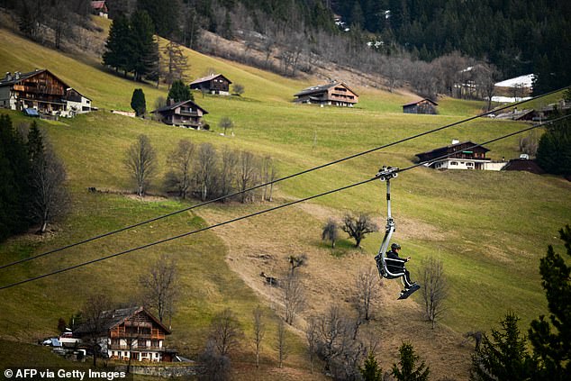 A snowboarder sits in a chair lift above a snowless landscape in La Clusaz resort near Annecy, southeastern France, on December 20,2025