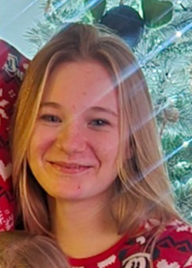 A young woman smiling, with blonde hair, wearing a red Christmas sweater.