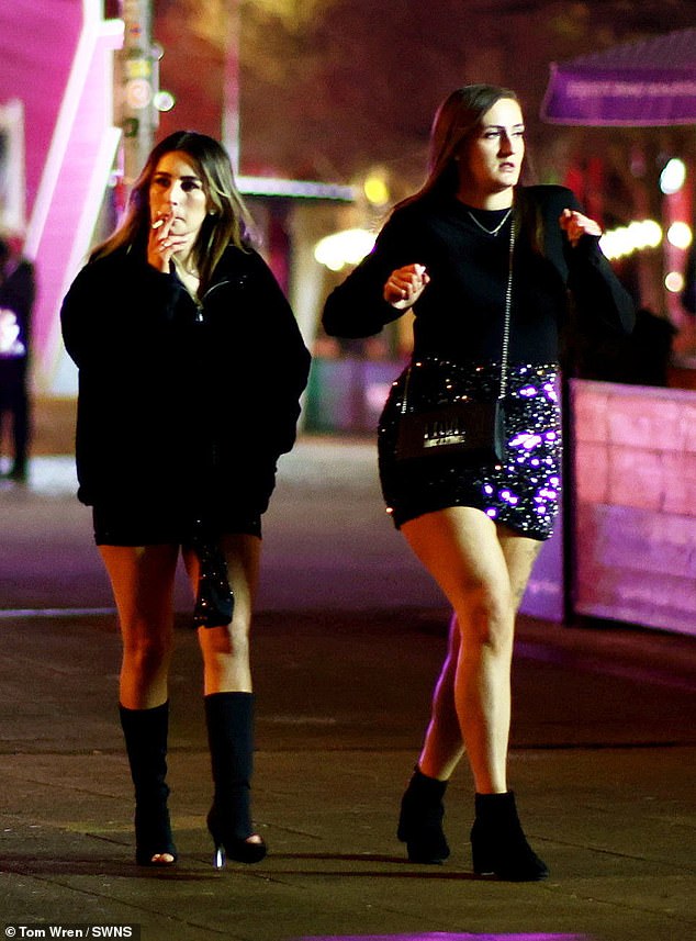 One woman smokes a cigarette as she walks with her friend in Bristol on New Year's Eve