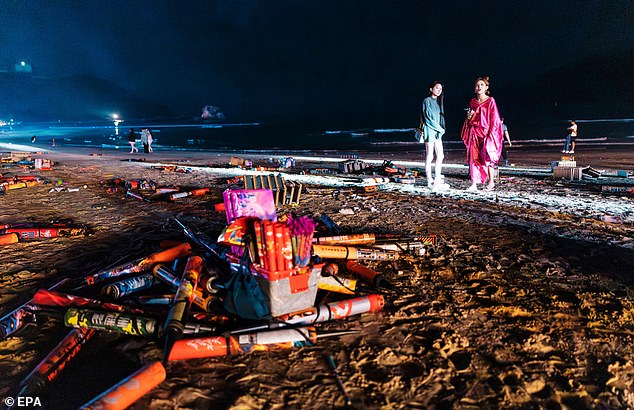 People stand among used firework shells on the beach during the 2026 New Year celebrations