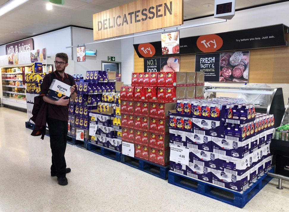 A man holds a pack of Corona beer next to pallets of Easter eggs in a supermarket.