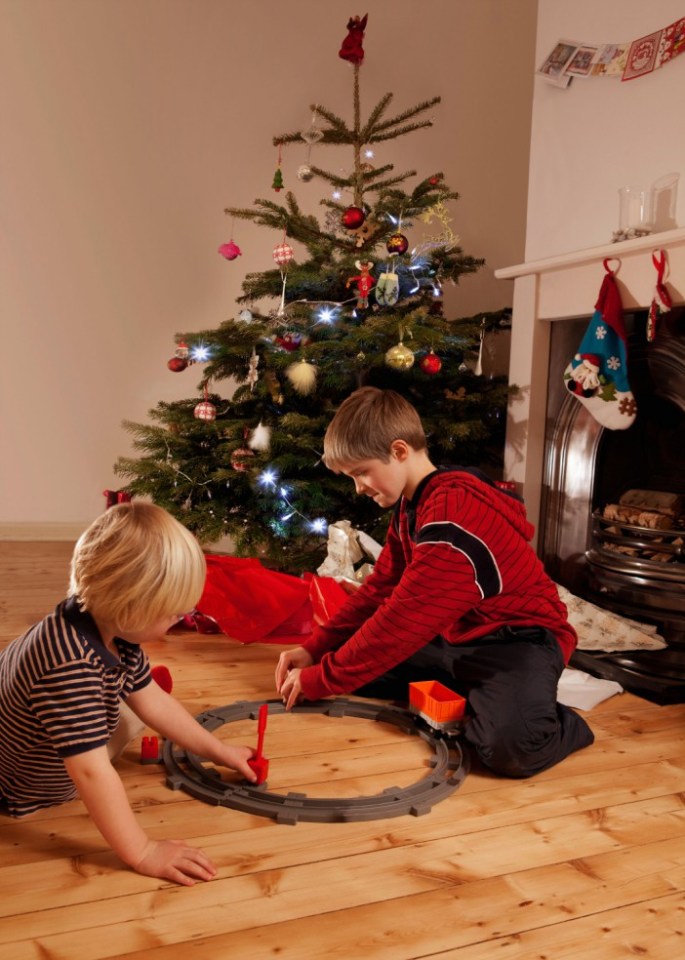 Two boys playing with a toy train set in front of a Christmas tree.