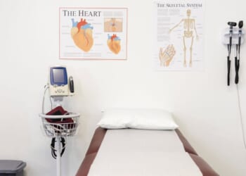 A clean, empty room in a doctor's office with an examination table and various pieces of medical equipment.