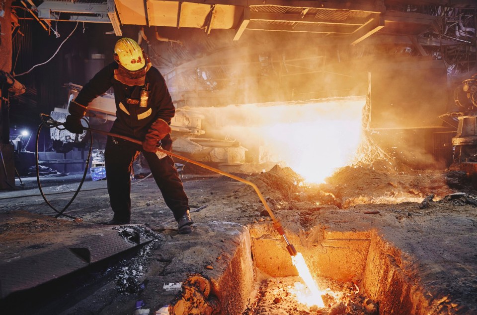 A worker in protective gear using a long tool to direct molten metal at Scunthorpe Steel Works.