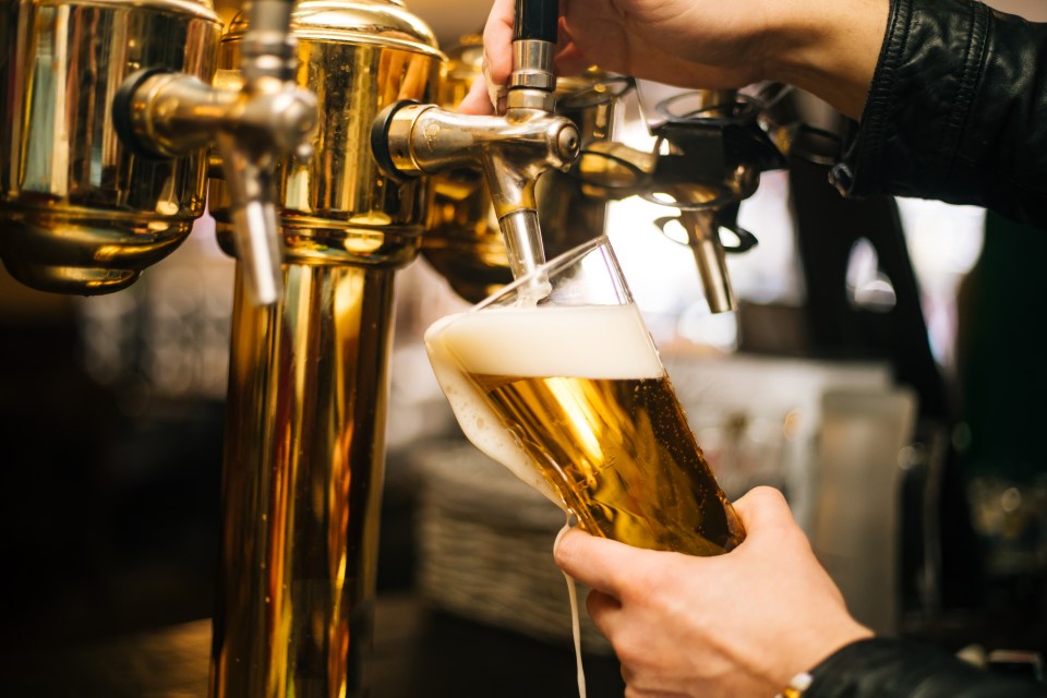 A bartender pouring beer from a tap into a glass, with foam spilling over the side.