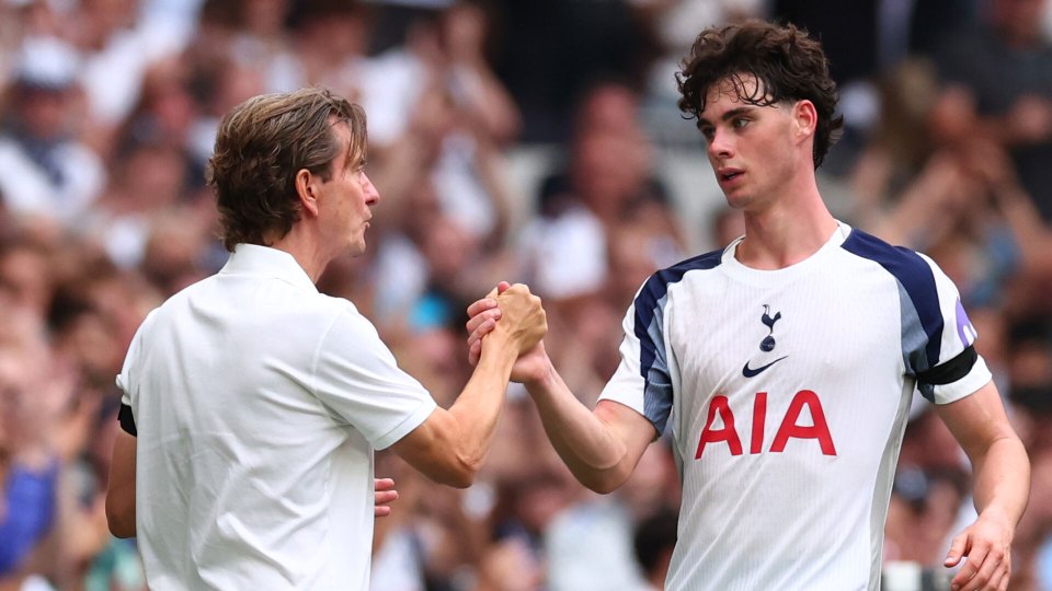 A man in a white polo shirt shaking hands with a younger man in a white and blue soccer jersey.