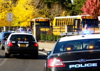 Police cars are parked near the entrance of a High School.