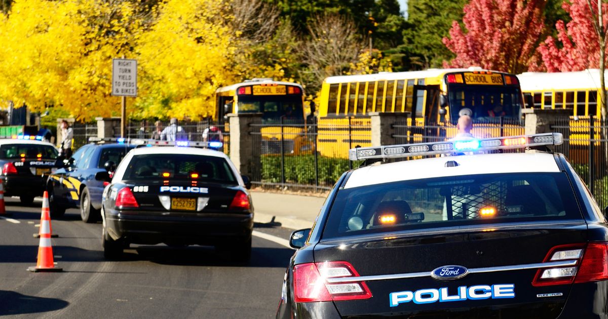 Police cars are parked near the entrance of a High School.