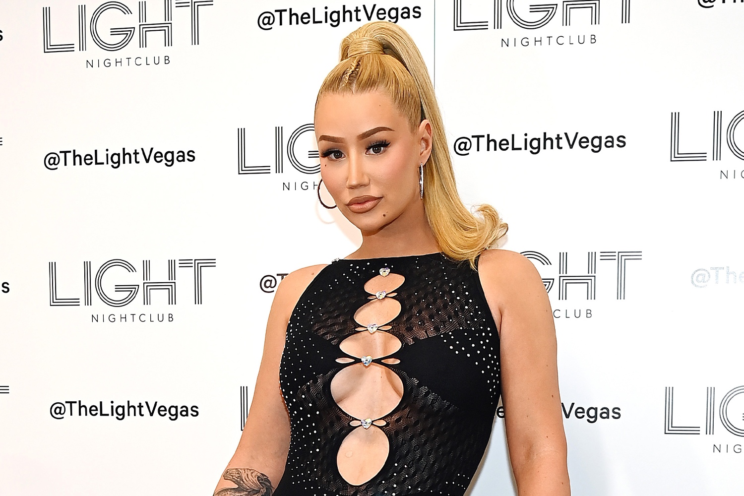 Iggy Azalea posing in a black mesh dress with cutouts against a "Light Nightclub" backdrop.