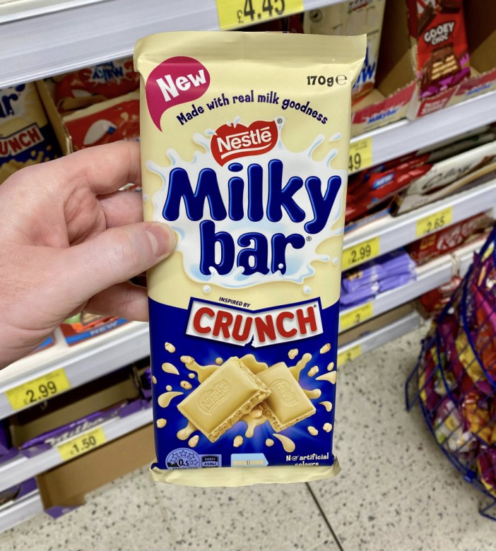 A hand holding a "Milky Bar Inspired by Crunch" chocolate bar package.