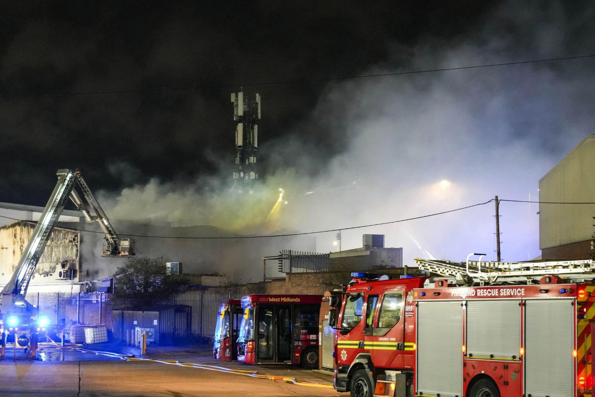 An image collage containing 1 images, Image 1 shows Firefighters battle a large fire at a food factory at night, with smoke billowing and emergency vehicles, including an elevated platform, surrounding the building