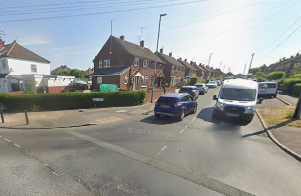 A neighborhood street with a row of brick houses on the right and cars parked along the curb.