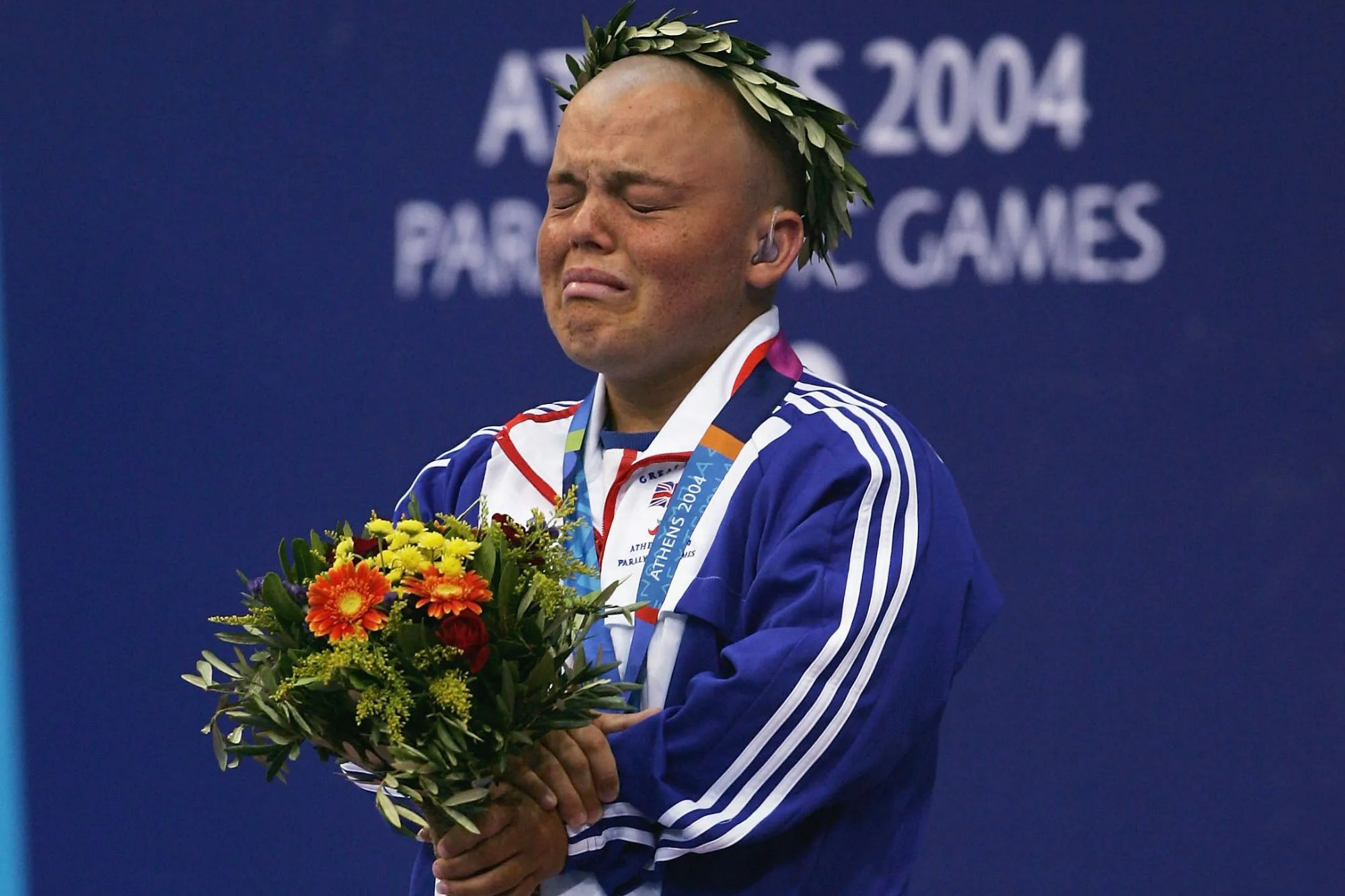 An image collage containing 1 images, Image 1 shows Paralympic gold medalist Gareth Duke crying while holding a bouquet of flowers and wearing a laurel wreath