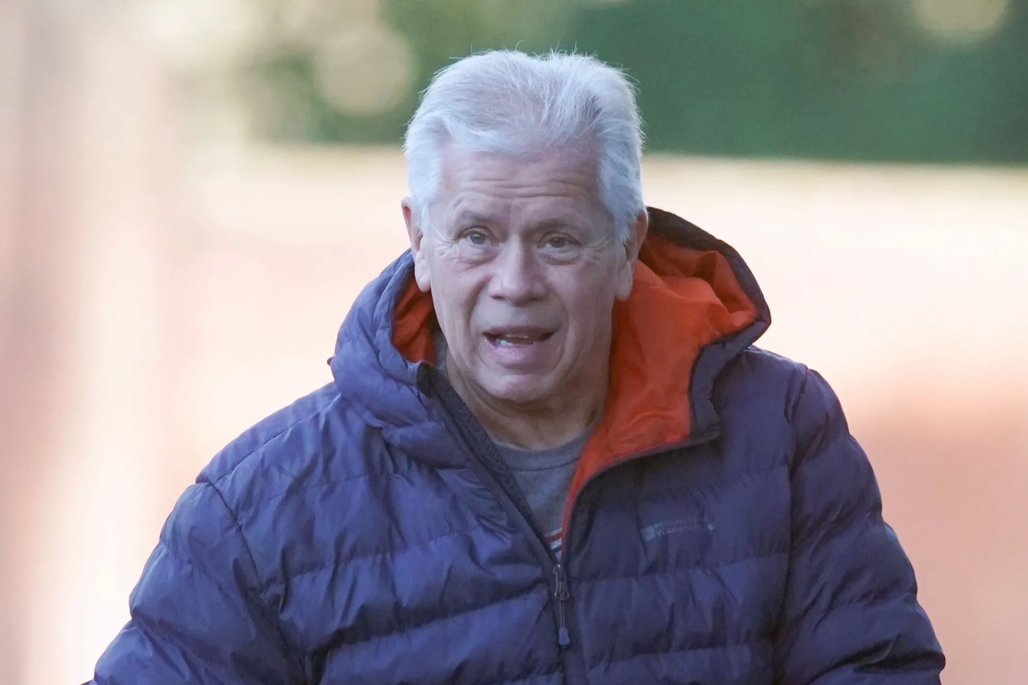 An image collage containing 1 images, Image 1 shows Mark Gibbon walking outdoors in a blue puffer jacket with an orange lining, gray T-shirt, grey camouflage pants, and black gloves, holding a dog leash
