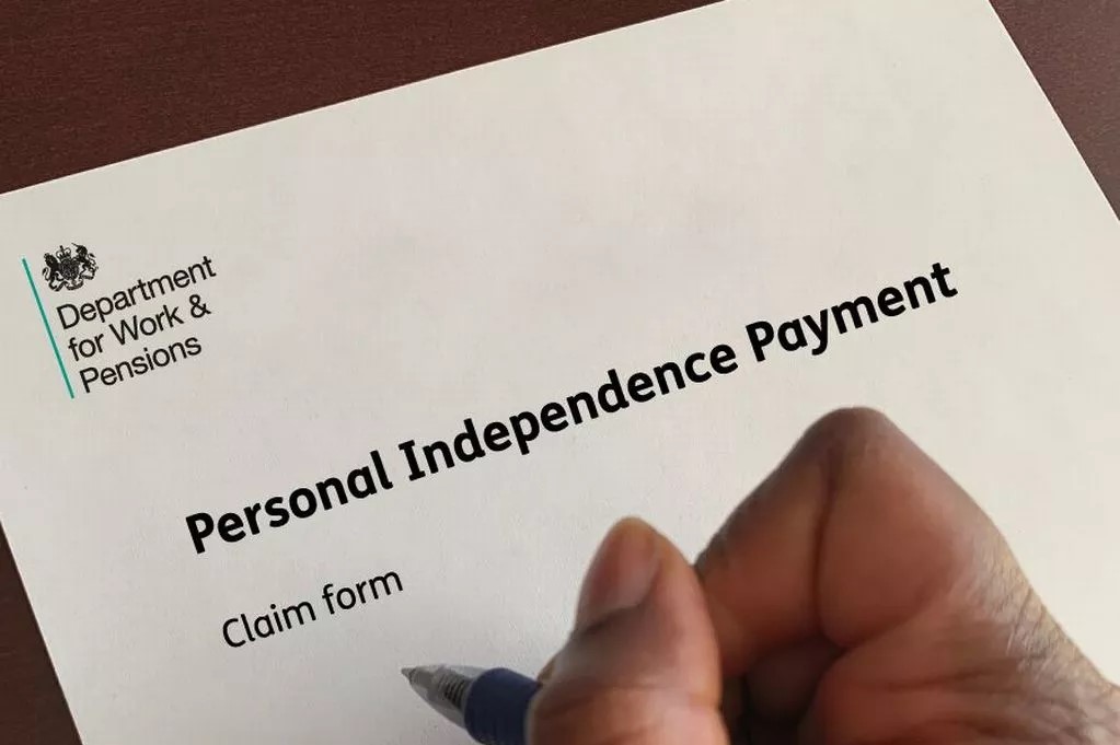 A person's hand filling out a Personal Independence Payment claim form from the Department for Work & Pensions.