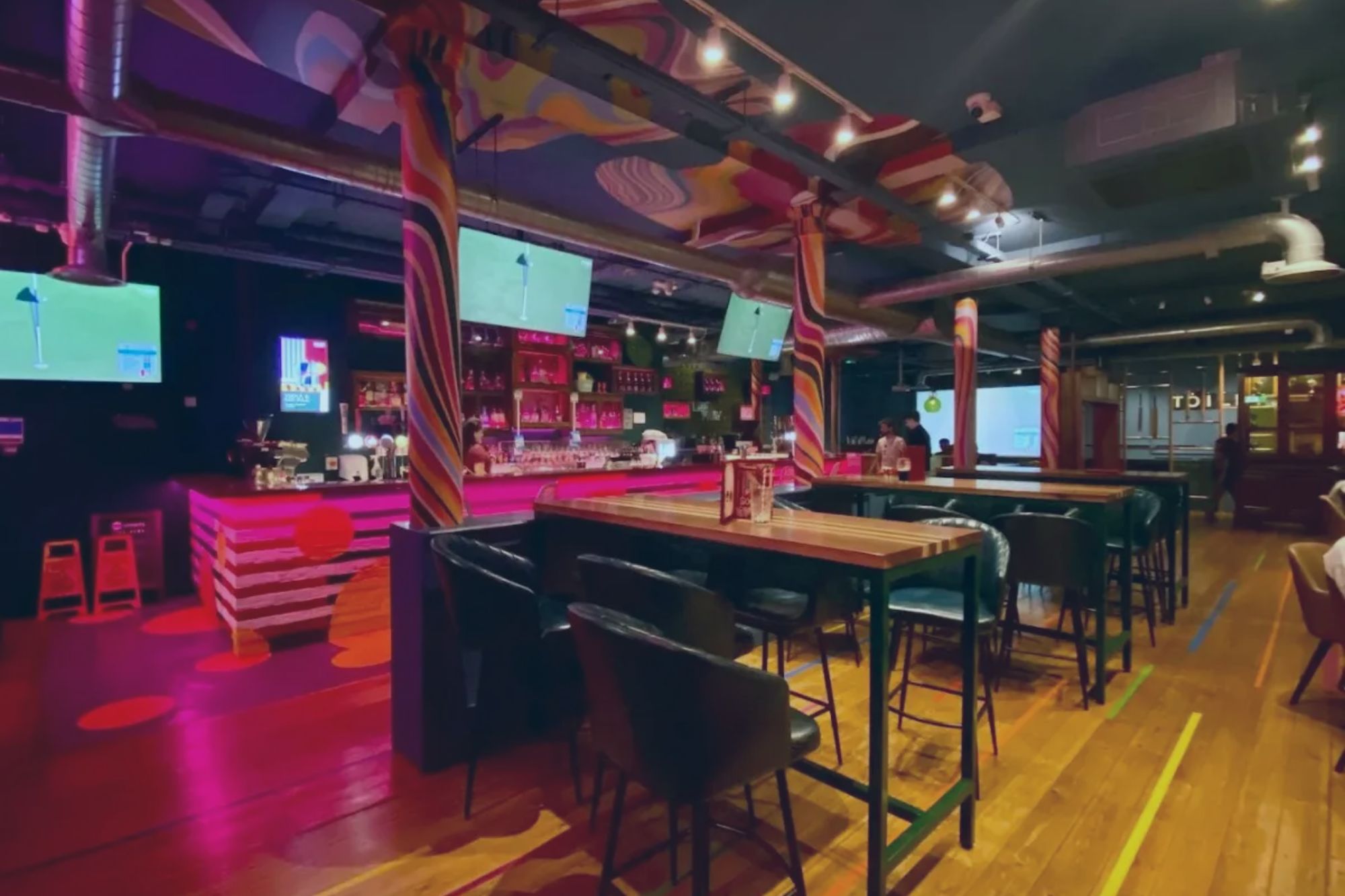 An image collage containing 1 images, Image 1 shows Interior of a modern bar with pink lighting, a colorful ceiling, and high-top tables