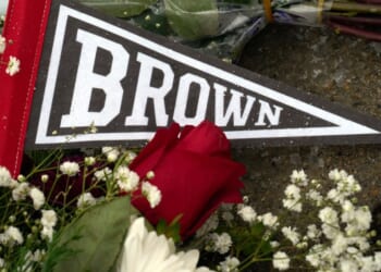A Brown University pennant is covered by flowers left by mourners at a makeshift memorial on the campus of Brown University, in Providence, Rhode Island, after a mass shooting Saturday that left two people dead and nine others wounded.