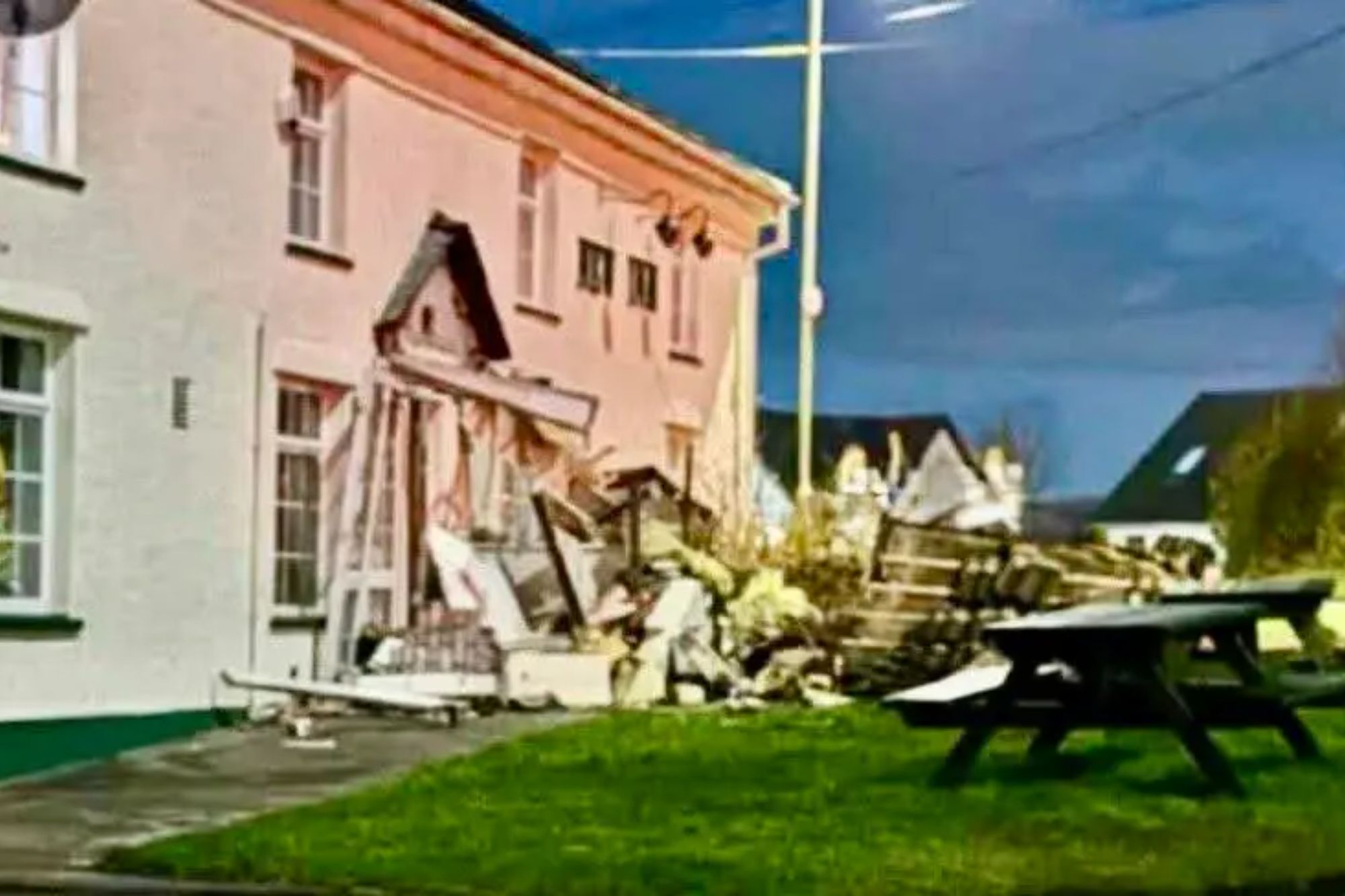 Damage to the front of a white building, possibly a pub, with debris scattered on the ground.