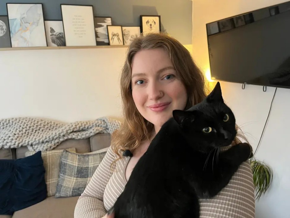 A woman holding a black cat on her shoulder.