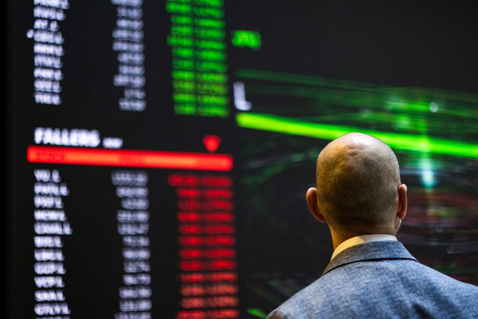A man in a suit looking at a digital board displaying stock prices with "FALLERS" highlighted in red.