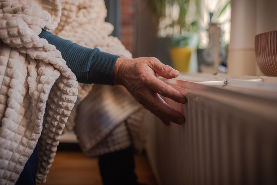 A person's hand in a red sleeve touches a white radiator to feel for heat.