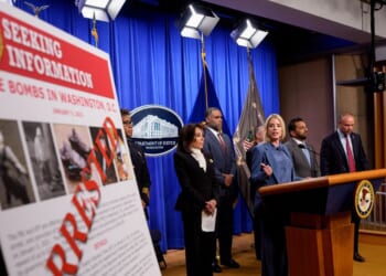 A poster reads "ARRESTED" in bold letters as Attorney General Pam Bondi speaks during a news conference on an arrest of a suspect in the January 6th pipe bomb case at the Department of Justice on Dec. 4, 2025, in Washington, D.C.