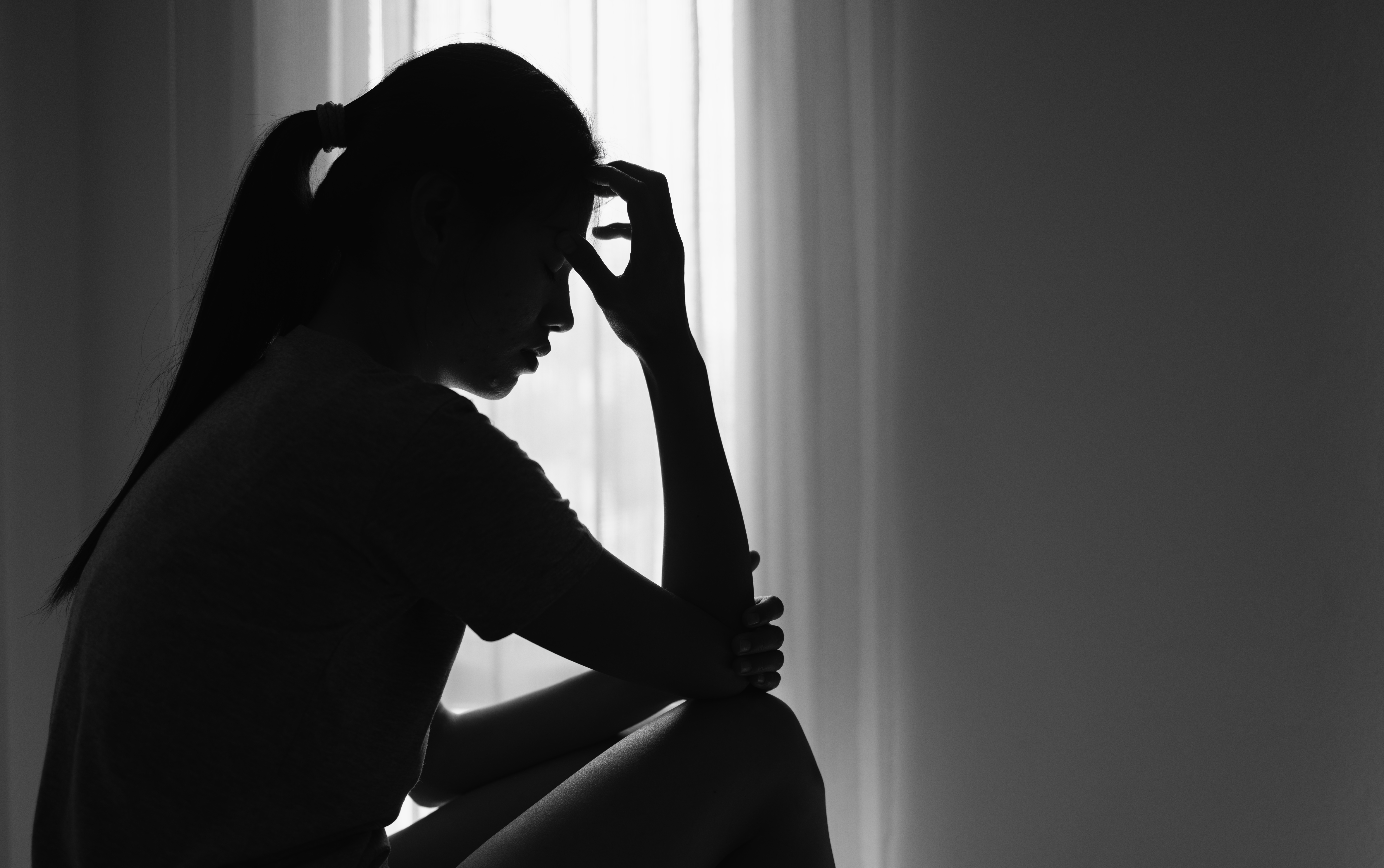 Silhouette of a woman in distress, her hand touching her forehead, symbolizing a deep sense of pain, anxiety, and sadness.