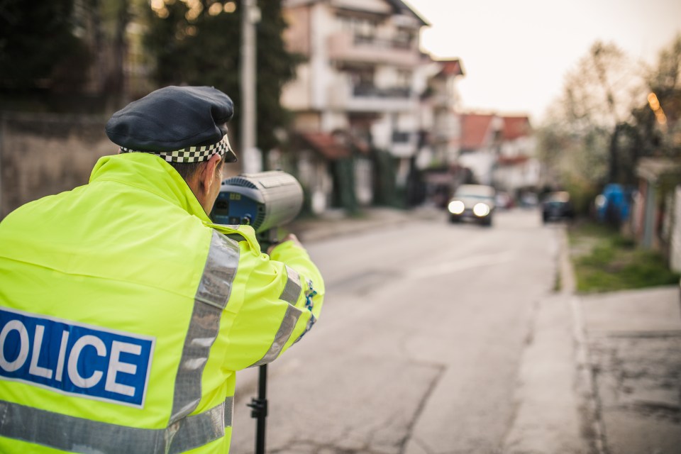 Police officer in a high-visibility jacket operating a speed camera towards oncoming traffic.