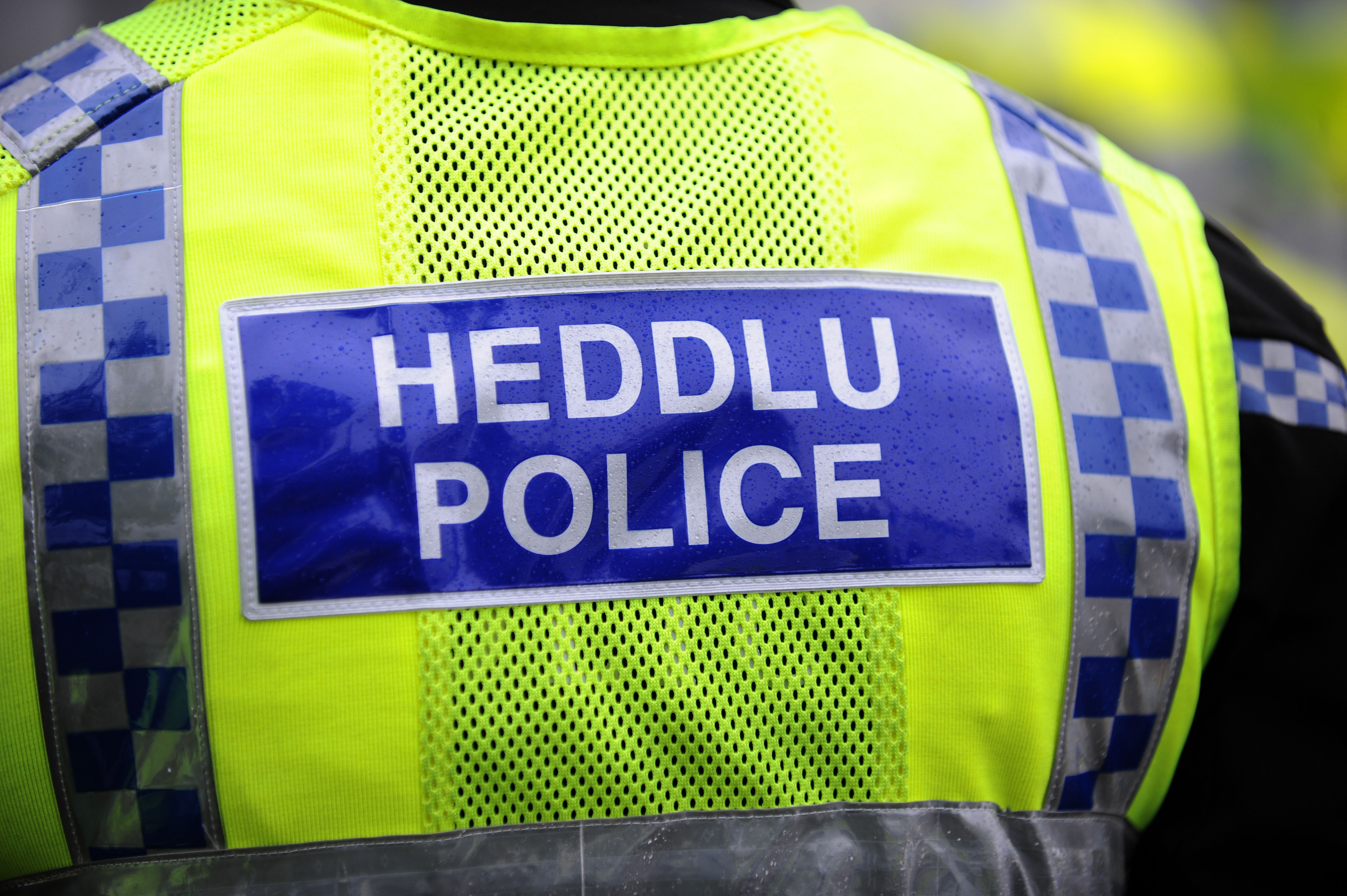 Back of a Welsh police officer's high-visibility vest with "HEDDLU POLICE" printed on it.