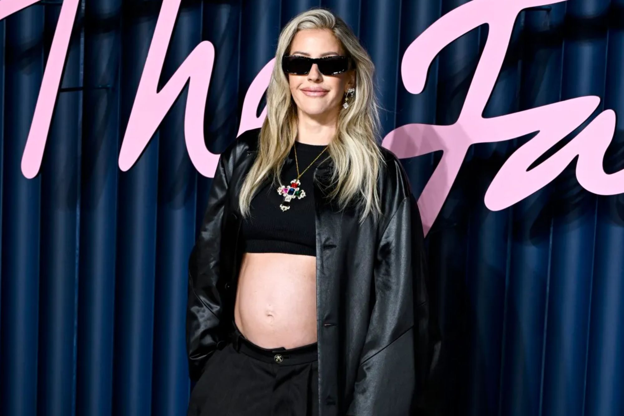 An image collage containing 1 images, Image 1 shows Pregnant woman in a black crop top, open black coat, and black pants with dark sunglasses