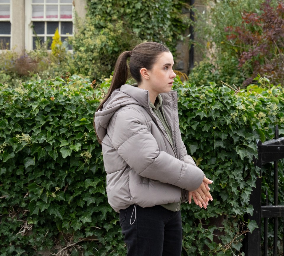 Young woman with dark hair in a ponytail wearing a puffer jacket with hands clasped in front.