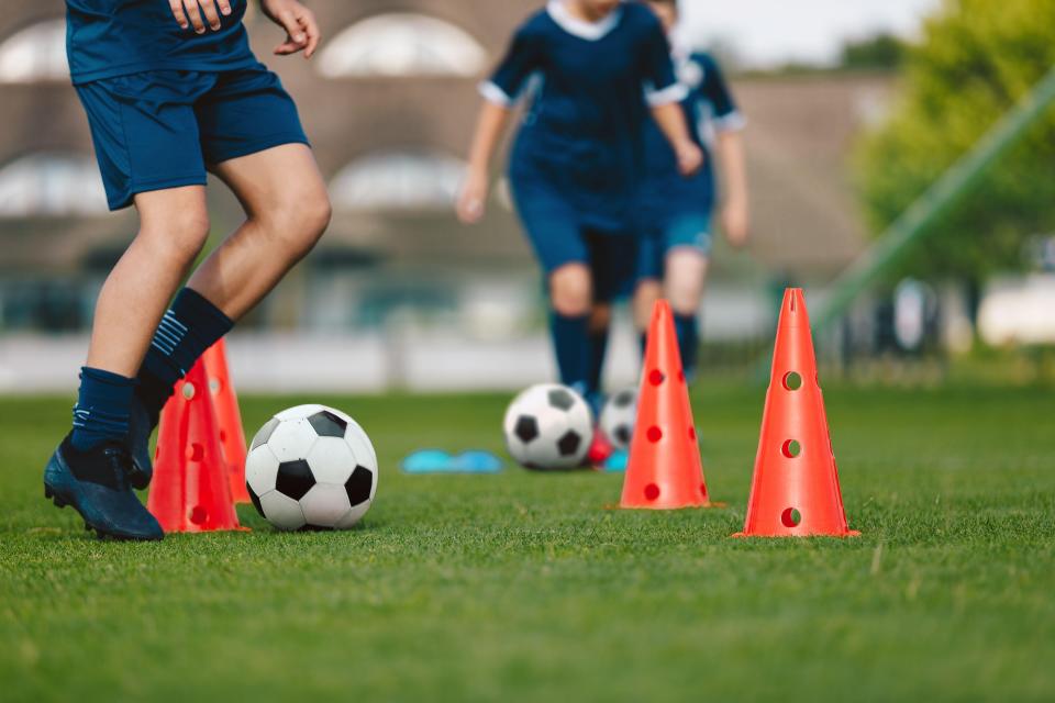 Children training with soccer balls and orange cones on a grassy field.