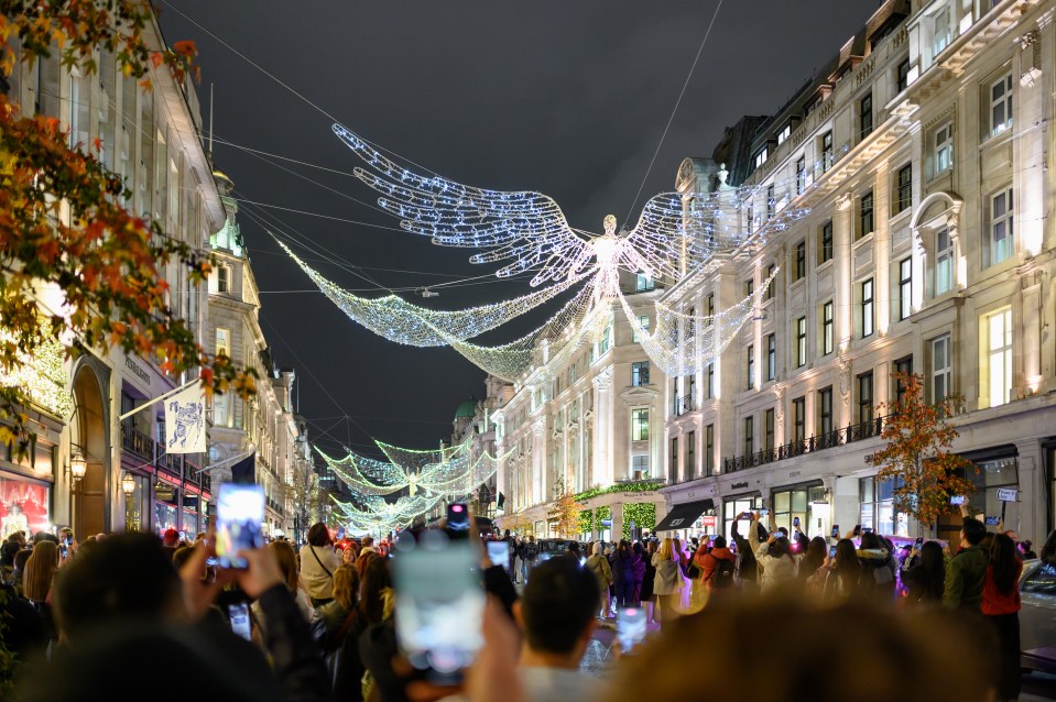 Christmas lights in the shape of angels illuminate Regent Street at night, with crowds taking photos.