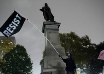 A protestor waves a flag in a pouring rain during a demonstration against an impending Customs and Border Patrol immigration crackdown in New Orleans on Dec. 1, 2025.