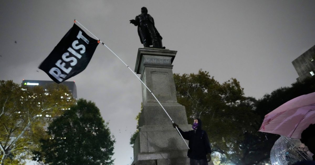 A protestor waves a flag in a pouring rain during a demonstration against an impending Customs and Border Patrol immigration crackdown in New Orleans on Dec. 1, 2025.