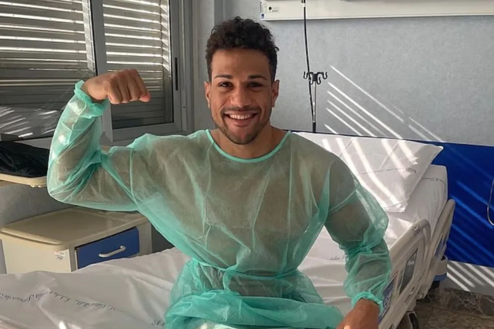 An image collage containing 1 images, Image 1 shows Fitness influencer Alessandro Antonicelli posing while sitting on a hospital bed, wearing a hospital gown