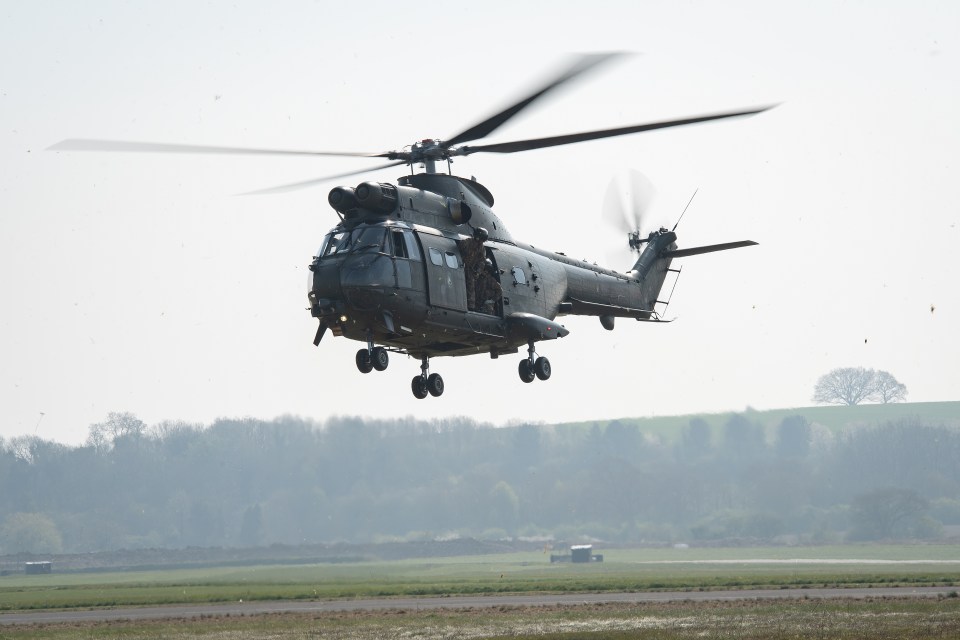 A Puma HC2 helicopter with crew members prepares to land on a runway.