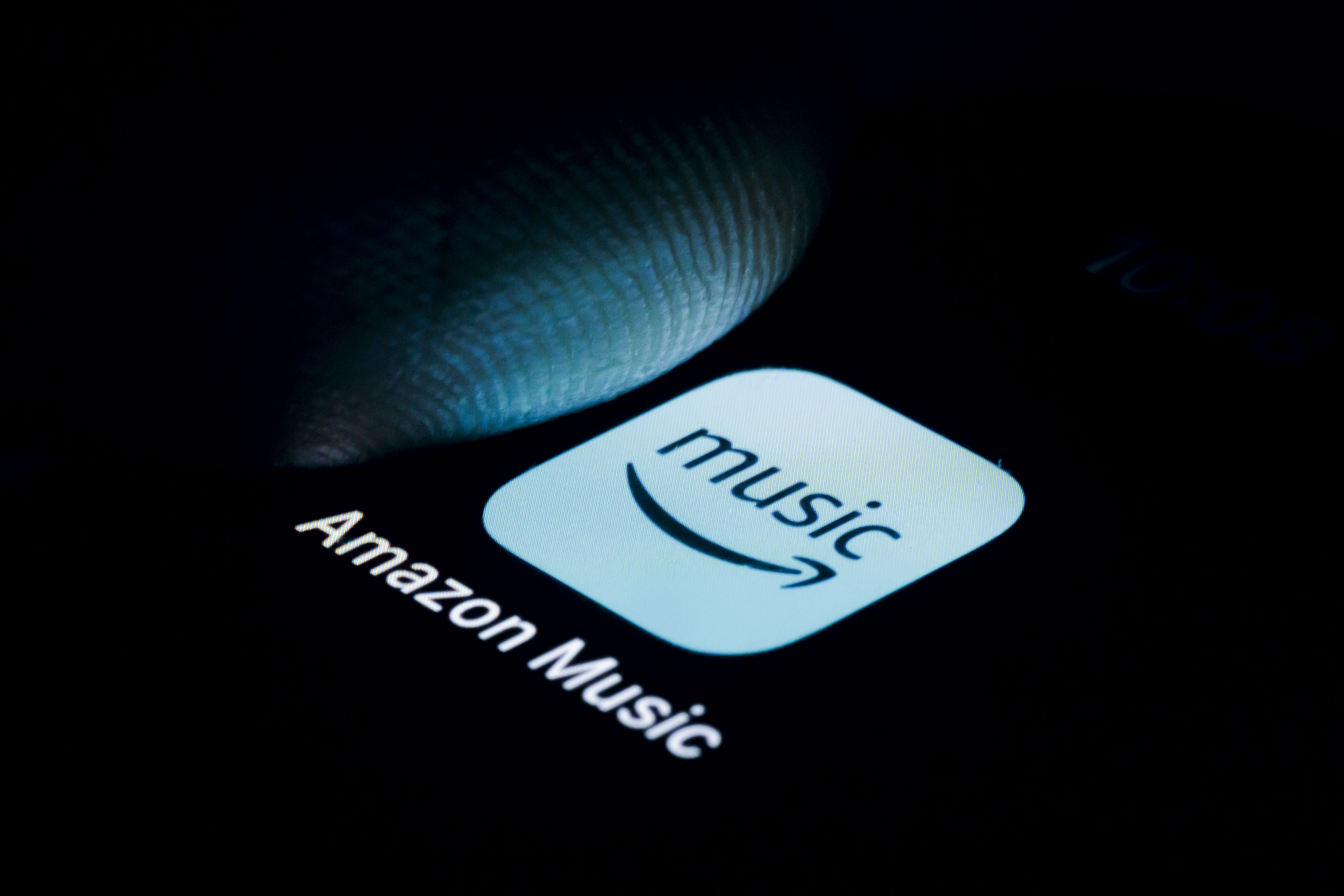 Photo illustration of the Amazon Music logo on a smartphone with a finger about to touch it.