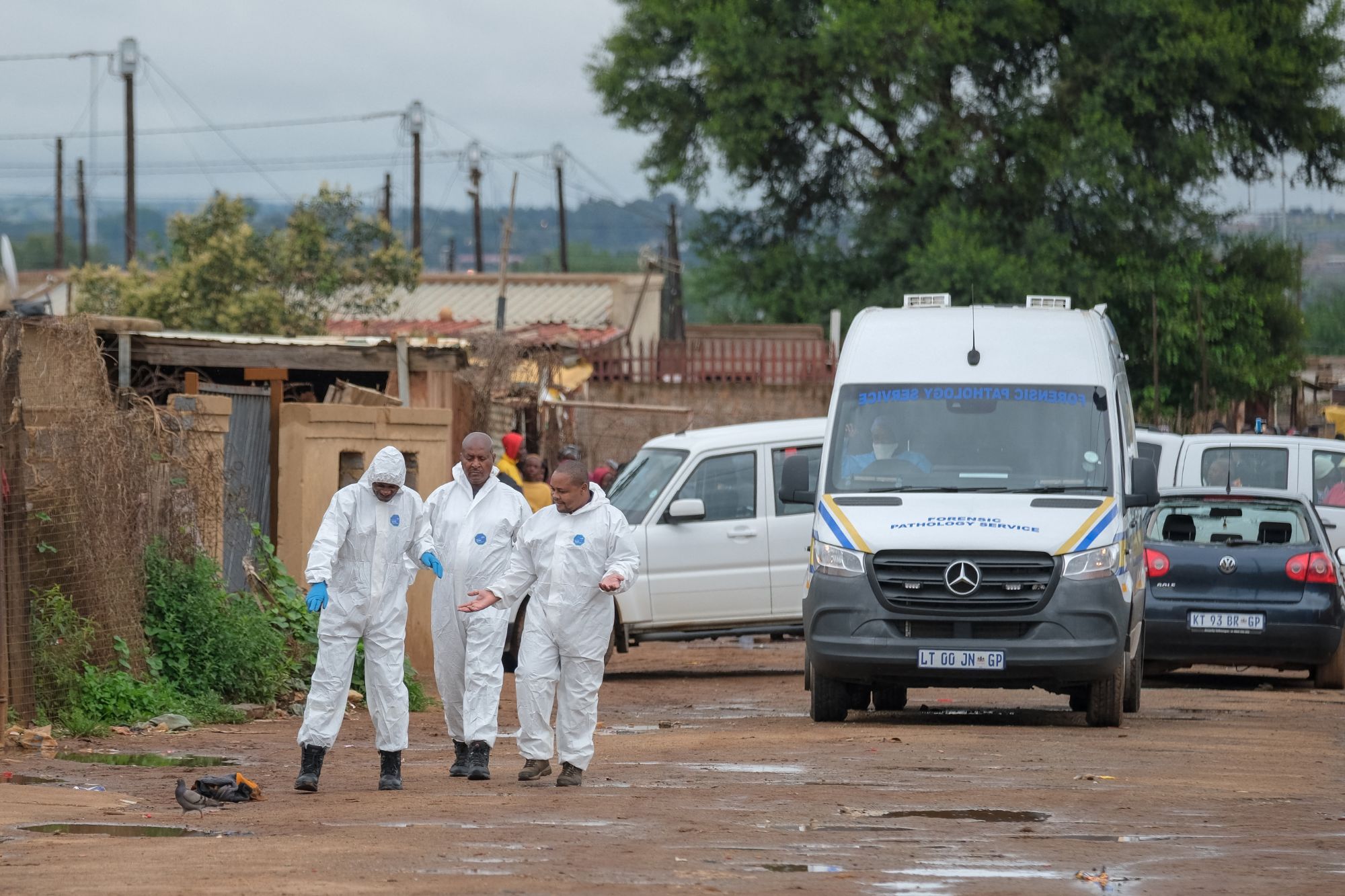 An image collage containing 1 images, Image 1 shows Forensic Pathology Service members in white suits walking at a crime scene