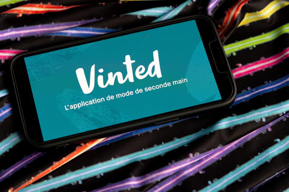 An iPhone displaying the Vinted logo and slogan on a colorful, vintage fabric background.