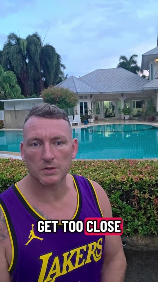 A man in a purple Lakers jersey standing in front of a pool and a clubhouse.