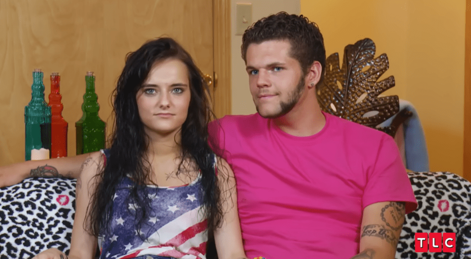 A woman in an American flag tank top and a man in a pink shirt sit on a leopard print couch.