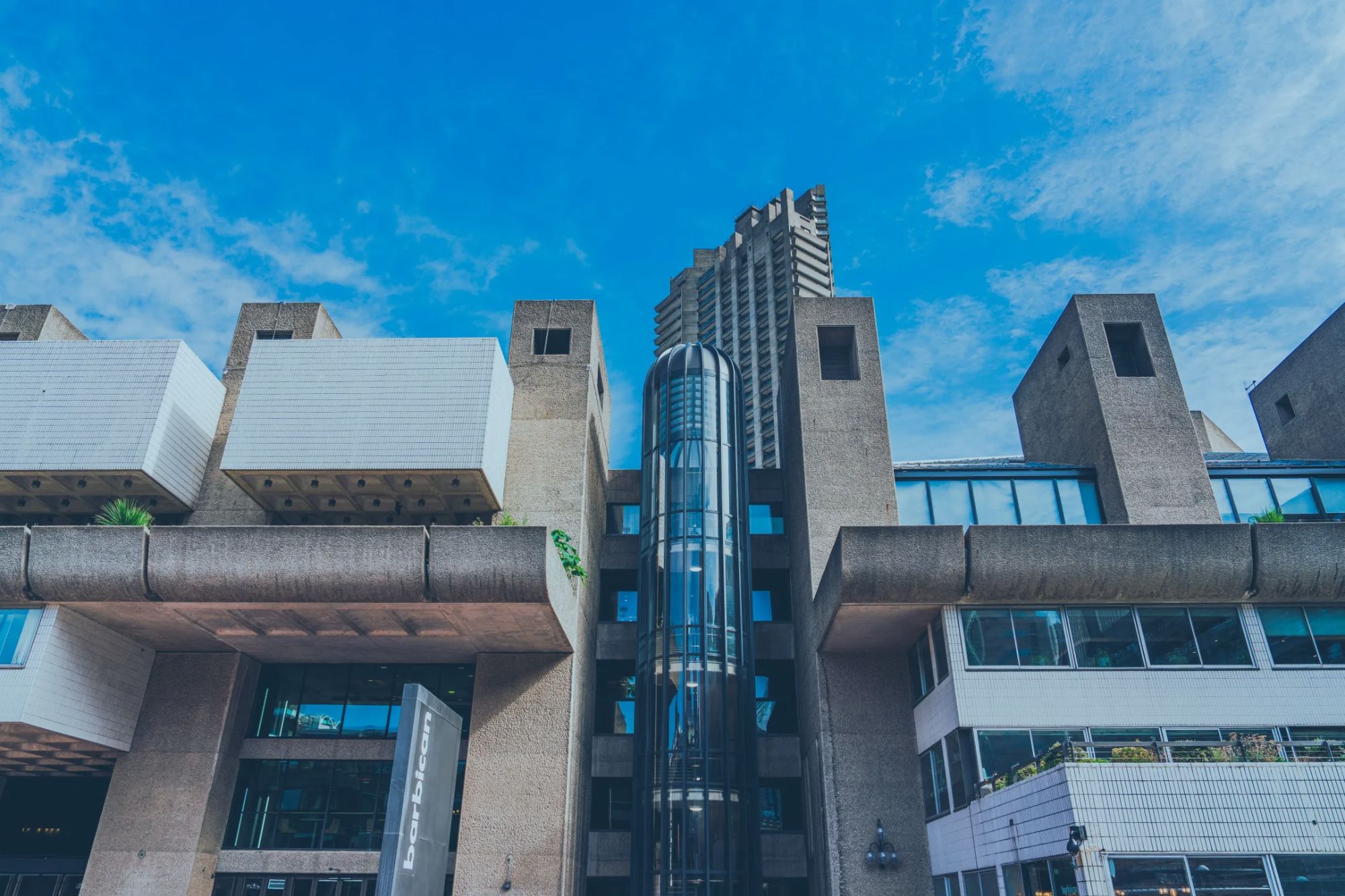 An image collage containing 1 images, Image 1 shows The exterior of the Barbican Centre building with a glass elevator