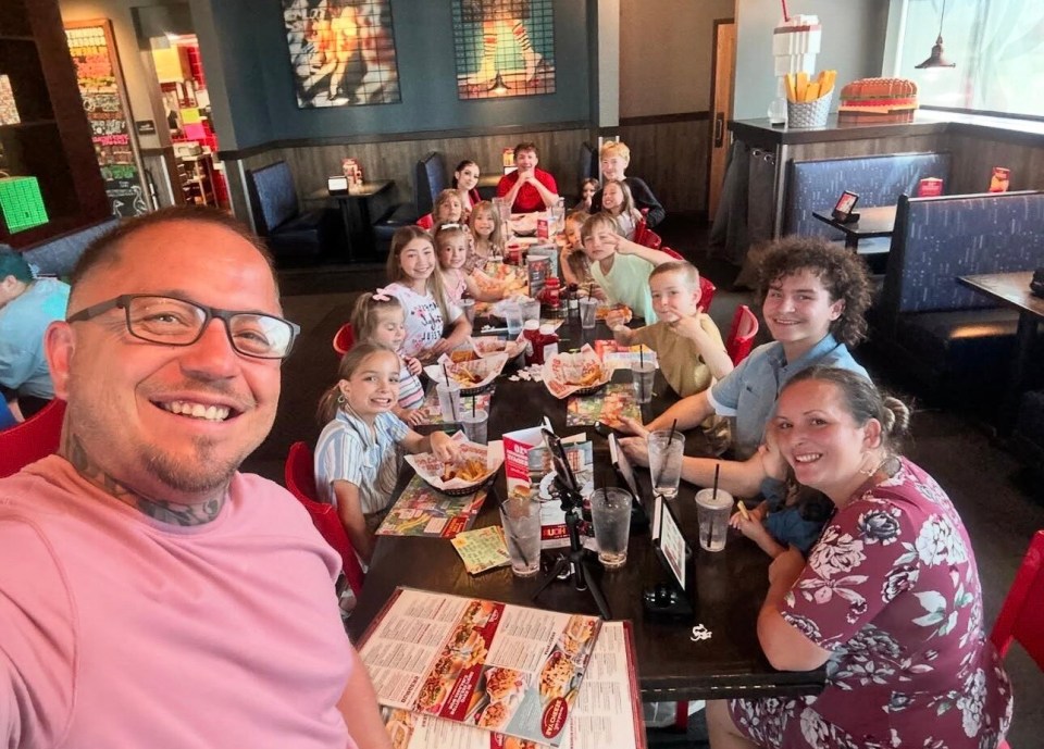 A large family with many children sitting at a long table in a restaurant.