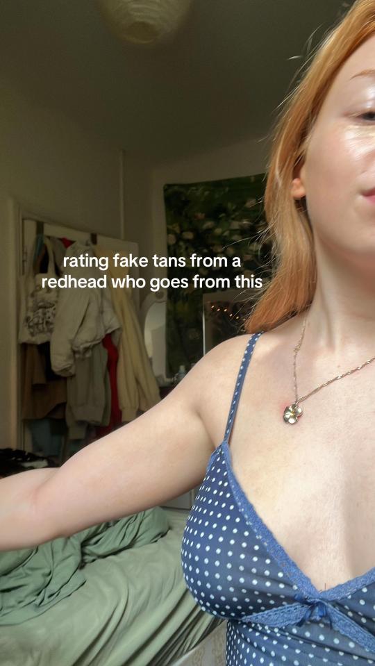 A woman with red hair and fair skin, wearing a blue polka dot top and a flower pendant, with text overlay: "rating fake tans from a redhead who goes from this".