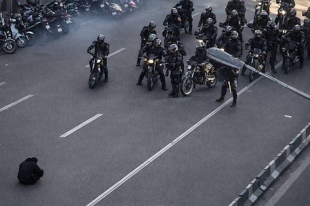 A photo of a lone demonstrator defiantly sitting on the road in front of armed security forces in Iran has gone viral on social media