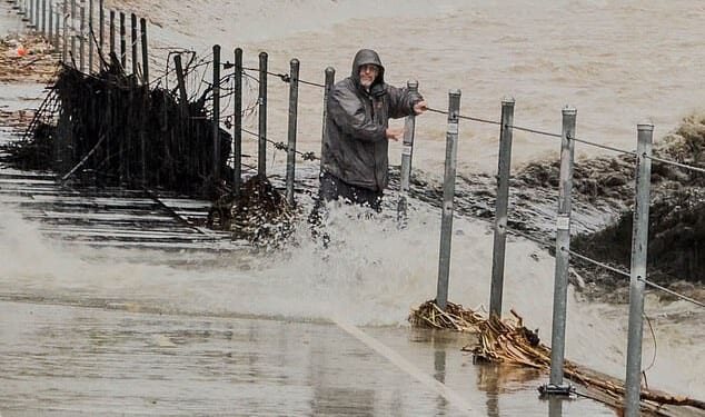 Thousands of California residents found themselves under evacuation orders on Christmas Eve, as disastrous floods and debris flows closed down roads. A man is pictured here hanging on to the railing for dear life after stepping into the path of a rushing culvert on Wednesday
