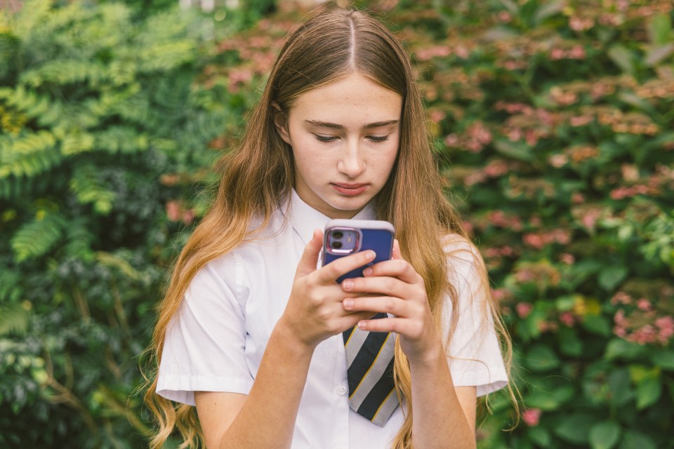Teenage schoolgirl in uniform looking at her smartphone.