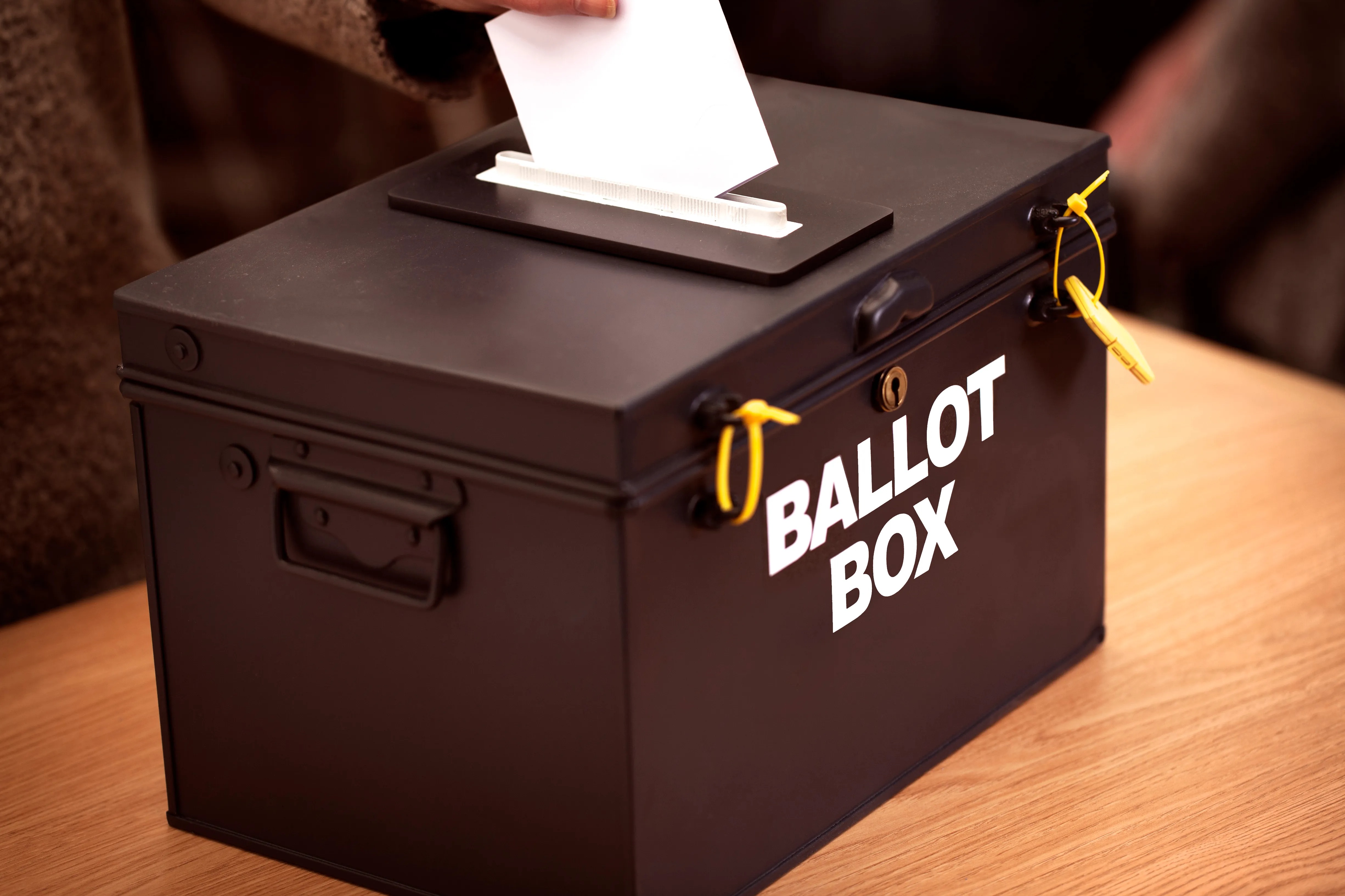 Person placing a vote into a black ballot box.