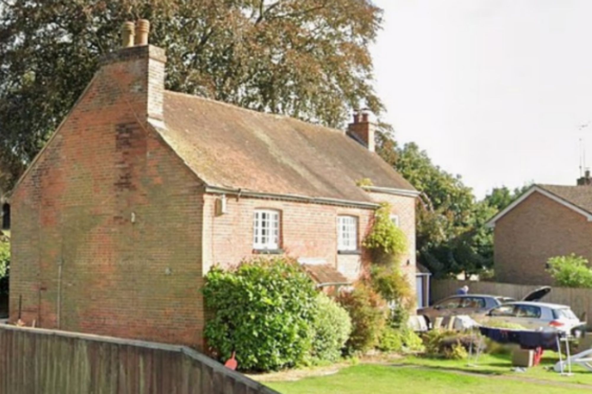 An image collage containing 1 images, Image 1 shows A brick cottage with two chimneys and white-framed windows, surrounded by trees and a garden with cars parked in the background